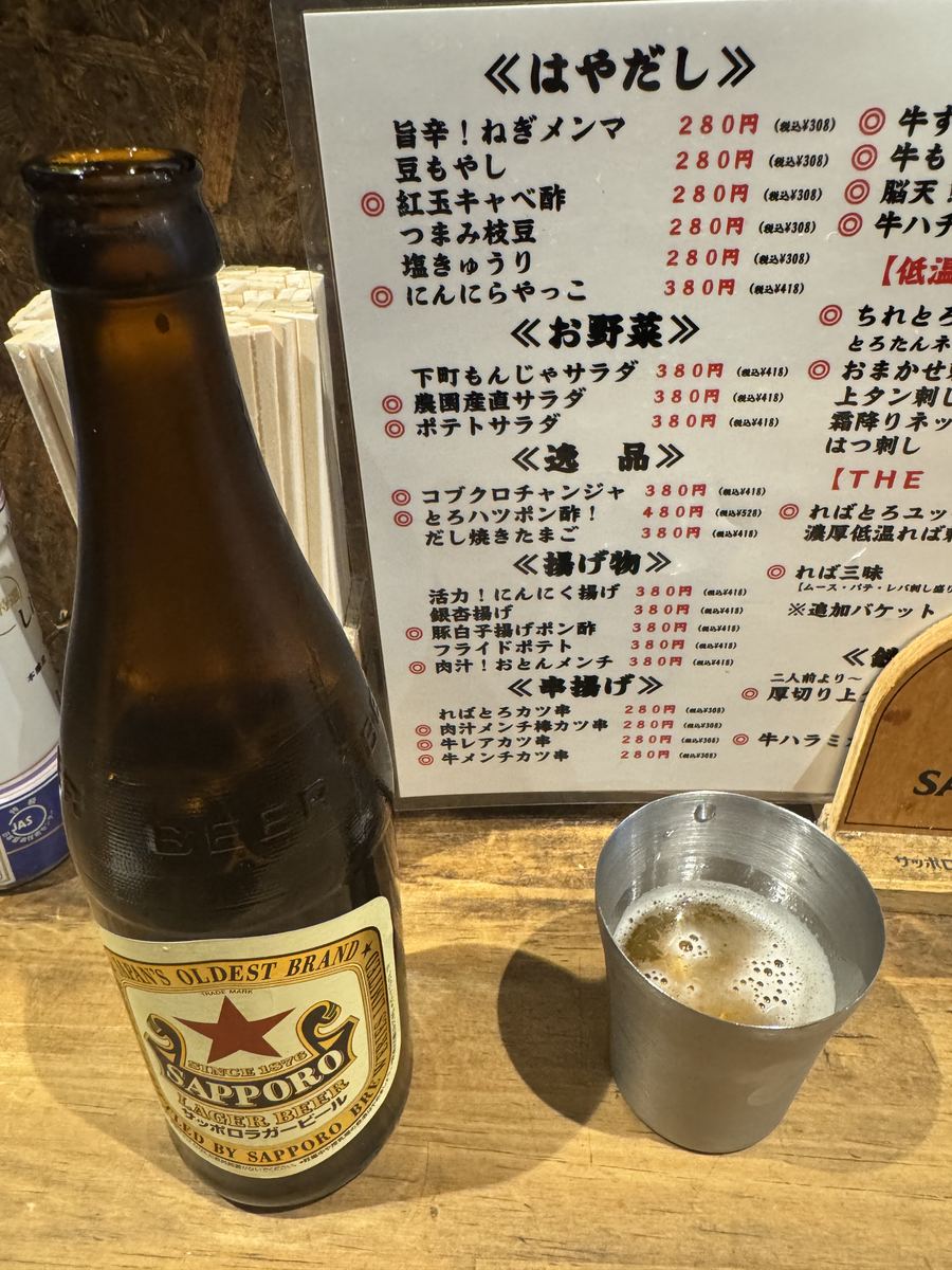 おとんばのサッポロ赤星の瓶ビールと、背後に並ぶメニュー表