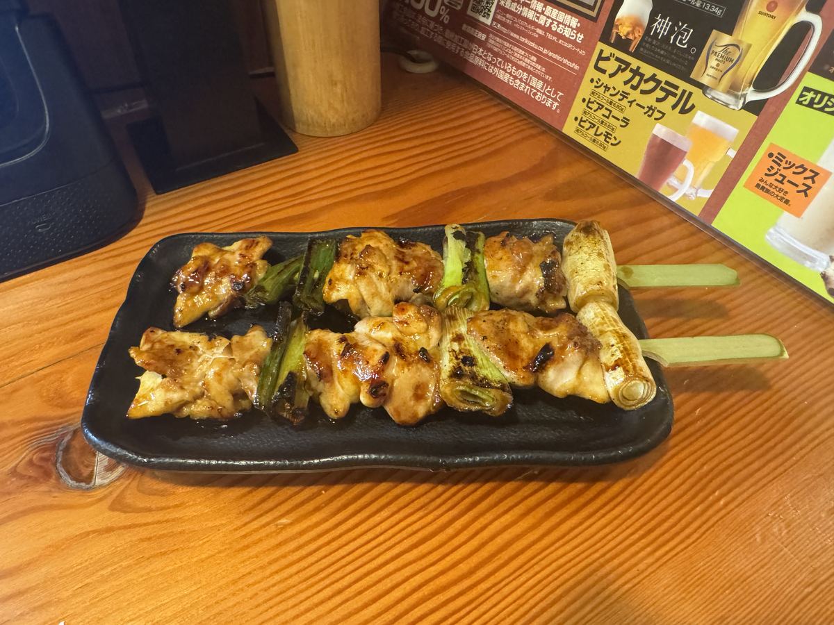 鳥貴族のもも貴族焼たれ。たれが絡んだ鶏もも肉の串焼きが黒い皿に並んでいる